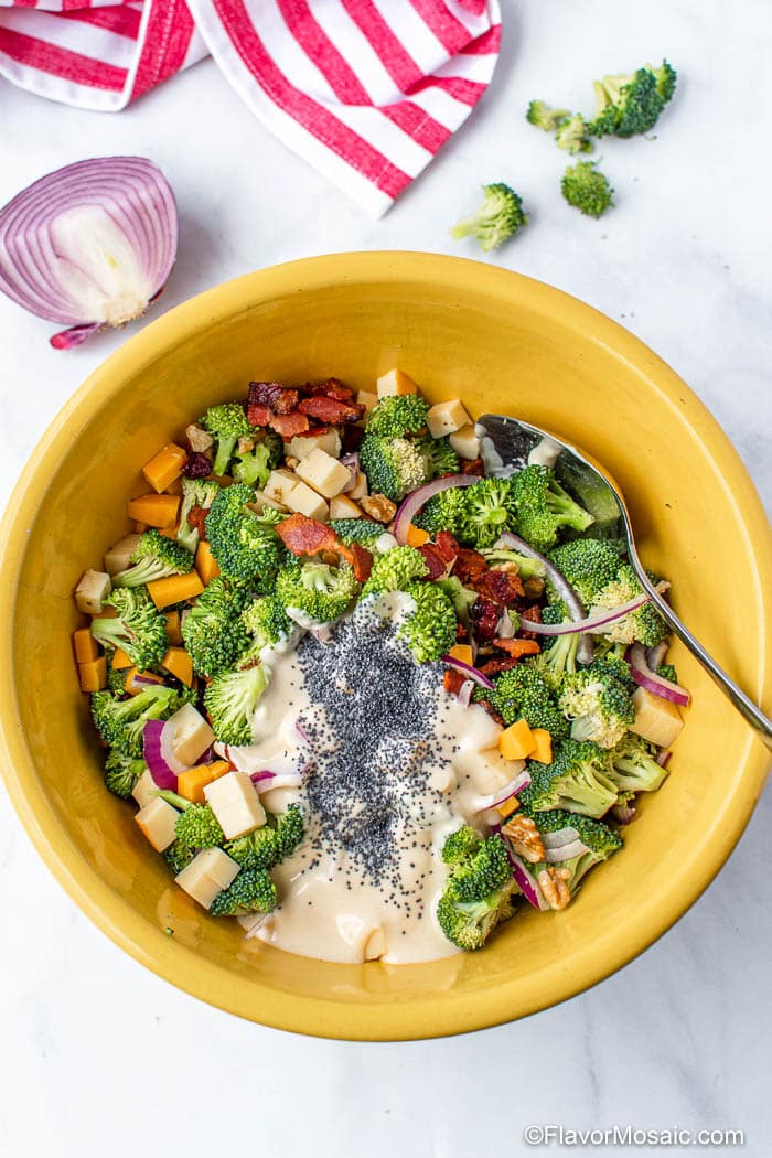 One large yellowish-gold bowl with ingredients of the broccoli salad mixed together except for the mayonnaise and poppyseeds.
