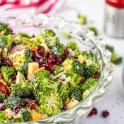 Photo of glass bowl with broccoli salad with cranberries, bacon and cheddar cheese on white marble countertop