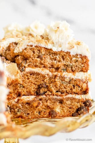 Close up view of the side of a slice of 3-layer homemade carrot cake with cream cheese frosting, and white marble background.