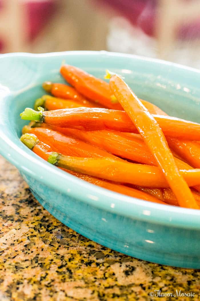 Thin Honey Glazed Carrots in a light blue bowl on a brown granite countertop.