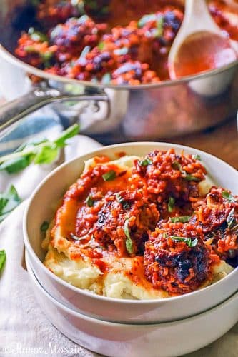 Bowl of mashed potatoes topped with porcupine meatballs and sauce.