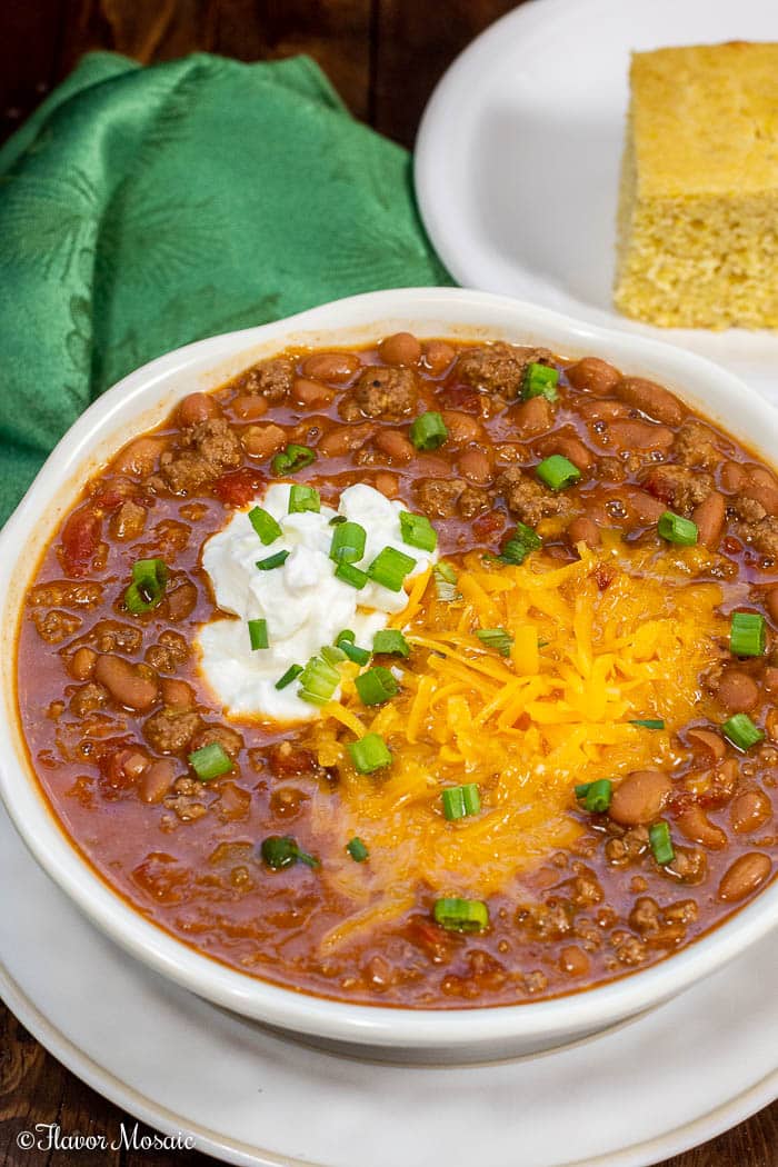 Big white bowl of Instant Pot Chili with shredded cheese green onions and sour cream.