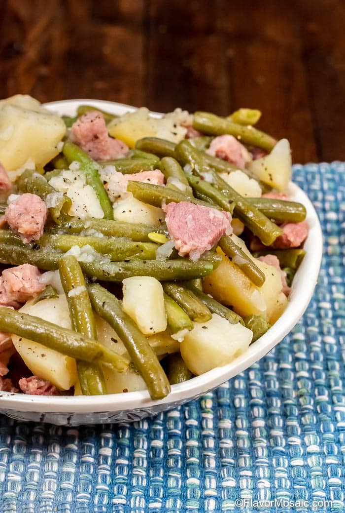 Photo of Instant Pot Ham Green Beans and Potatoes in white bowl on blue placemat on brown wood table.