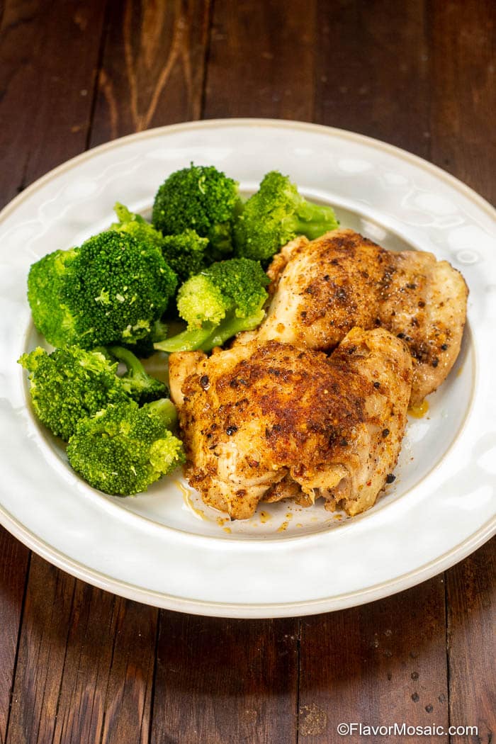 Two pieces of Instant Pot Chicken Thighs with broccoli on a white plate and dark wood table.