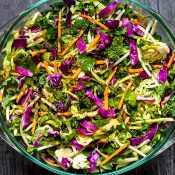 Glass bowl of Mexican Cabbage Slaw with Red Cabbage and carrots sitting on top of old gray barn wood table.