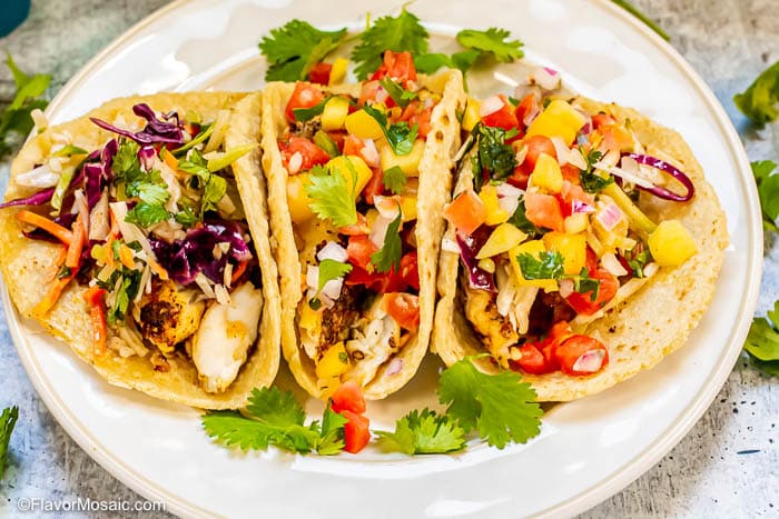 Horizontal photo of 3 fish tacos 1 with Mexican Cabbage Slaw and 2 others with Mango salsa