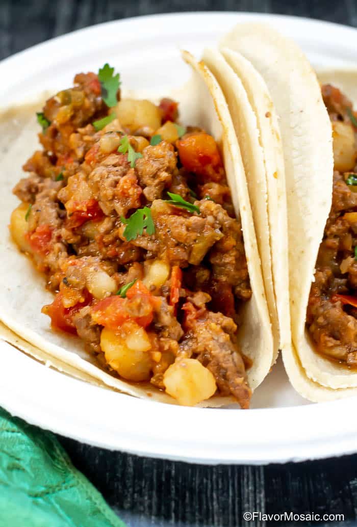 Vertical photo of corn tortillas filled with Picadillo (Tex-Mex Style) on a white plate.