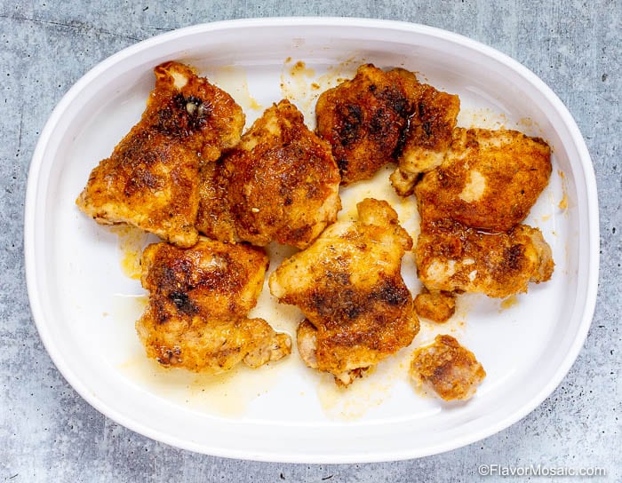 Several pieces of cooked Cajun Braised Chicken Without gravy in a white baking dish.