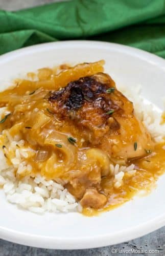 One serving of Cajun Braised Chicken With Gravy over rice on white plate with green napkin in the background.