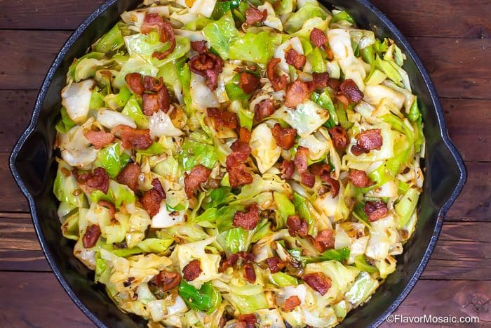 Horizontal overhead photo of Fried Cabbage with Bacon in a cast iron skillet on a wood table.