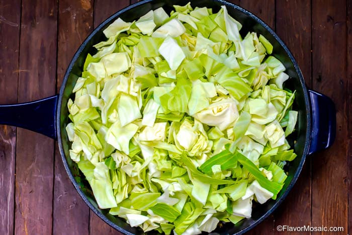 Overhead photo of cut up green cabbage in cast iron skillet on wood table.