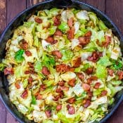 Overhead view of Fried Cabbage with Bacon in Skillet on wood table.