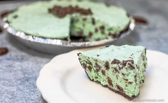 Horizontal photo of slice of Grasshopper pie, like a Chocolate Mint Pie, with the rest of the pie in the background.