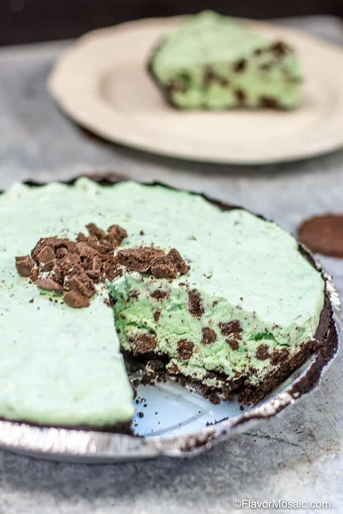 Grasshopper Pie, like chocolate mint pie, with one slice removed and placed on a white plate in background.