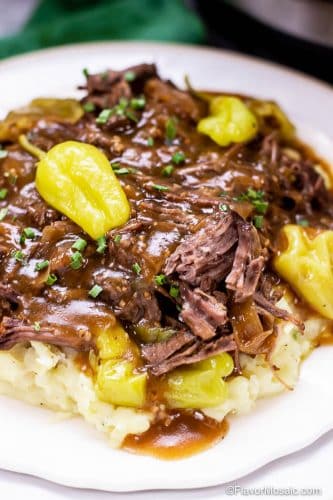 Serving of Instant Pot Mississippi Pot Roast over mashed potatoes on white plate.