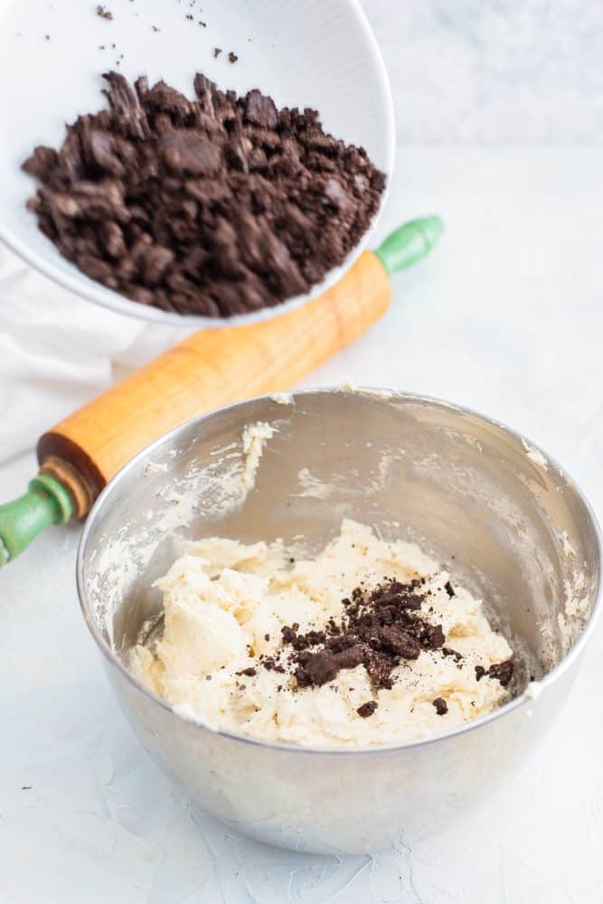 Process shot of bowl of crush Oreos rolling pin and bowl of cookie batter with a few Oreo crumbs