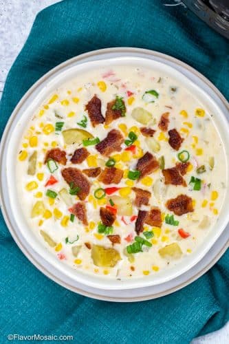 Overhead view of a white bowl of corn chowder topped with bacon and green onions sitting on a blue napkin.