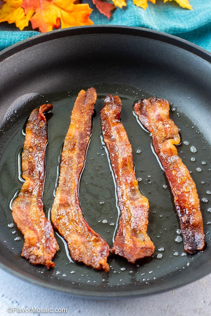 Skillet with 4 slices of cooked bacon in bacon grease.