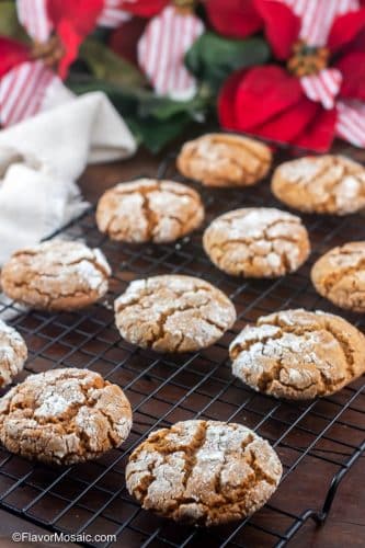 A Dozen Molasses Crinkle Cookies on a baking rack over a dark wood background with red and white bows and greenery in the background.