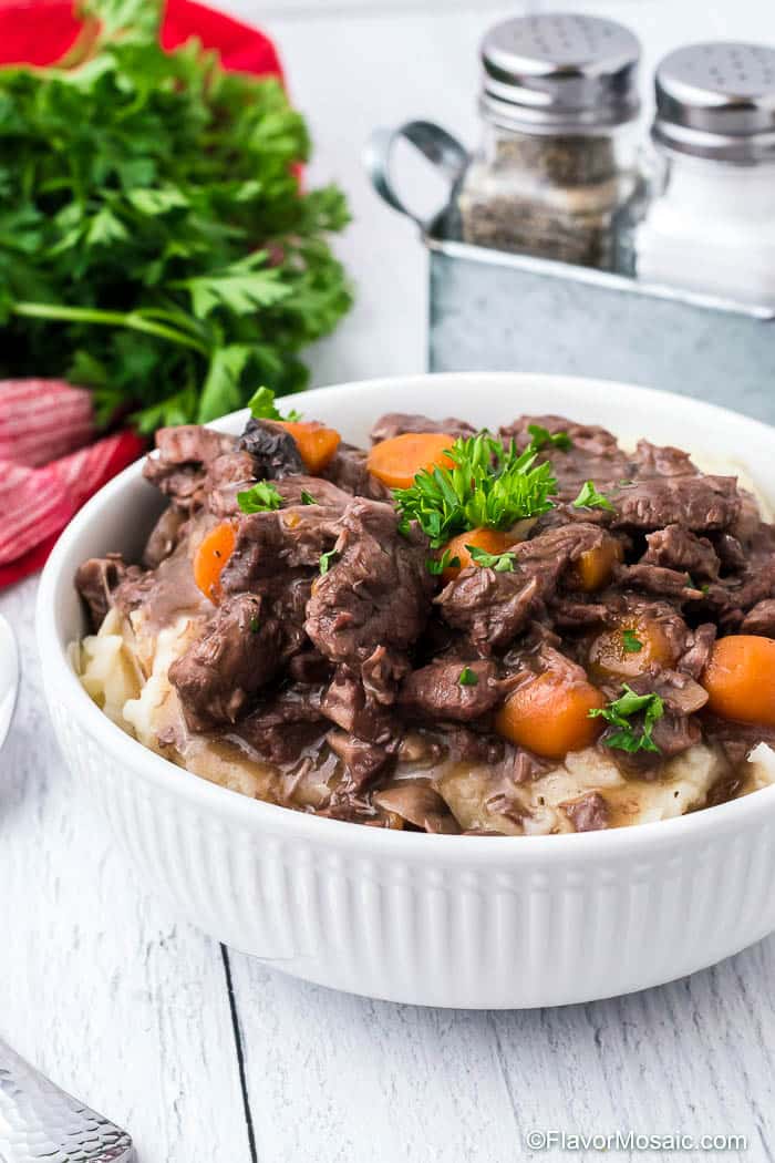 White bowl of Instant Pot Beef Burgundy with carrots and parsley over mashed potatoes.