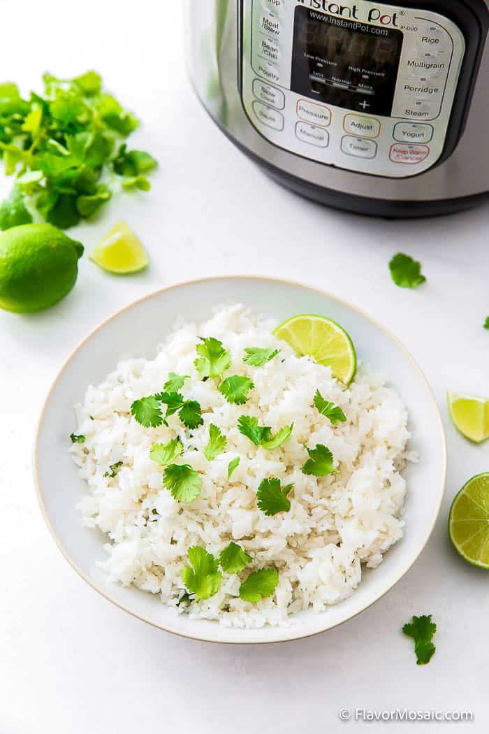 White Bowl of Cilantro Lime Rice with lime slice and surrounded by limes and cilantro in front of an Instant Pot.