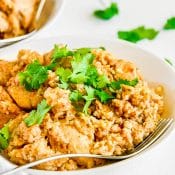 View of large white bowl of Instant Pot Chicken And Rice topped with chopped cilantro and surrounded by pieces of cilantro on white background with a partial view of another bowl of chicken and rice.