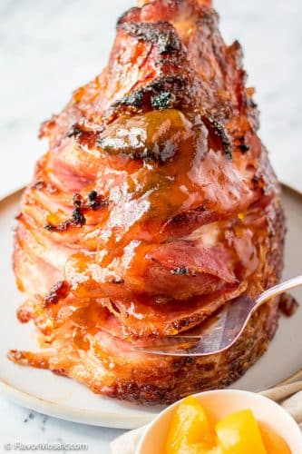 Straight on view of Peach Glazed Bone-In Spiral Ham with a partial view of a small bowl of sliced peaches in the bottom right of the photo.