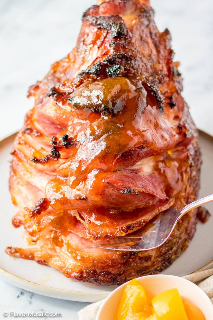 Straight on view of Peach Glazed Bone-In Spiral Ham with a partial view of a small bowl of sliced peaches in the bottom right of the photo.