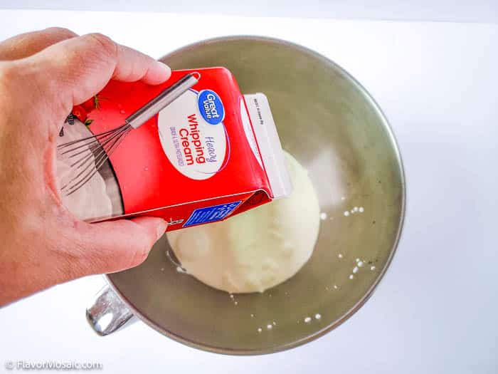 Overhead view of pouring heavy whipping cream into a metal bowl.