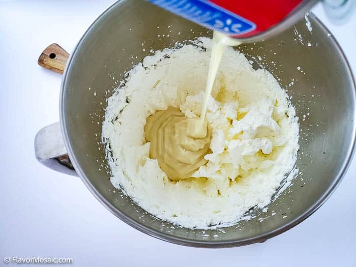 Overhead view of pouring sweetened condensed milk into a bowl with whipped cream.