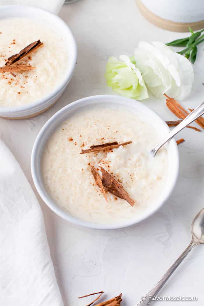 Overhead view of 2 bowls of rice pudding with cinnamon on a light gray / off white counter with white napkin.