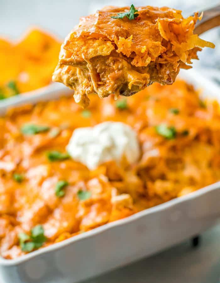 A spoonful of Chicken Dorito Casserole being held above the casserole dish with the rest of the chicken Dorito casserole.