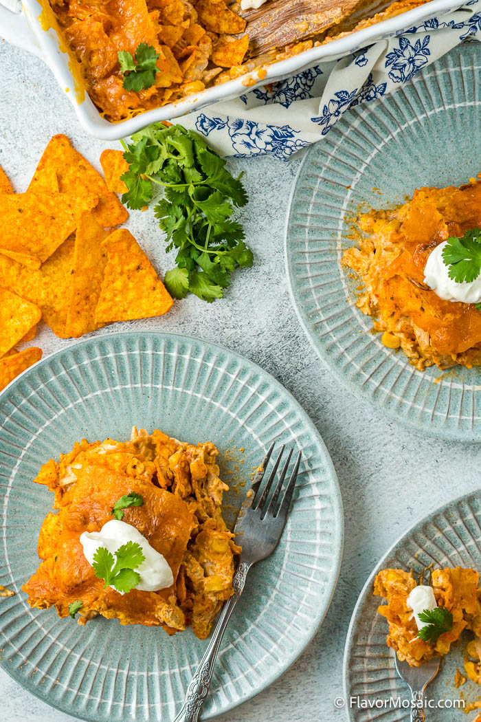 Overhead view of 2 aqua plates and partial view of a corner of another plate with the corner of the casserole dish at the top and individual Doritos on the table with sprigs of cilantro.