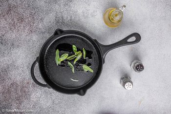 Sage leaves in a cast iron skillet with oil and salt and pepper on the side.
