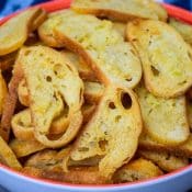 Close up photo of Buttery Garlic Bread Chips in a blue bowl with peach colored trim