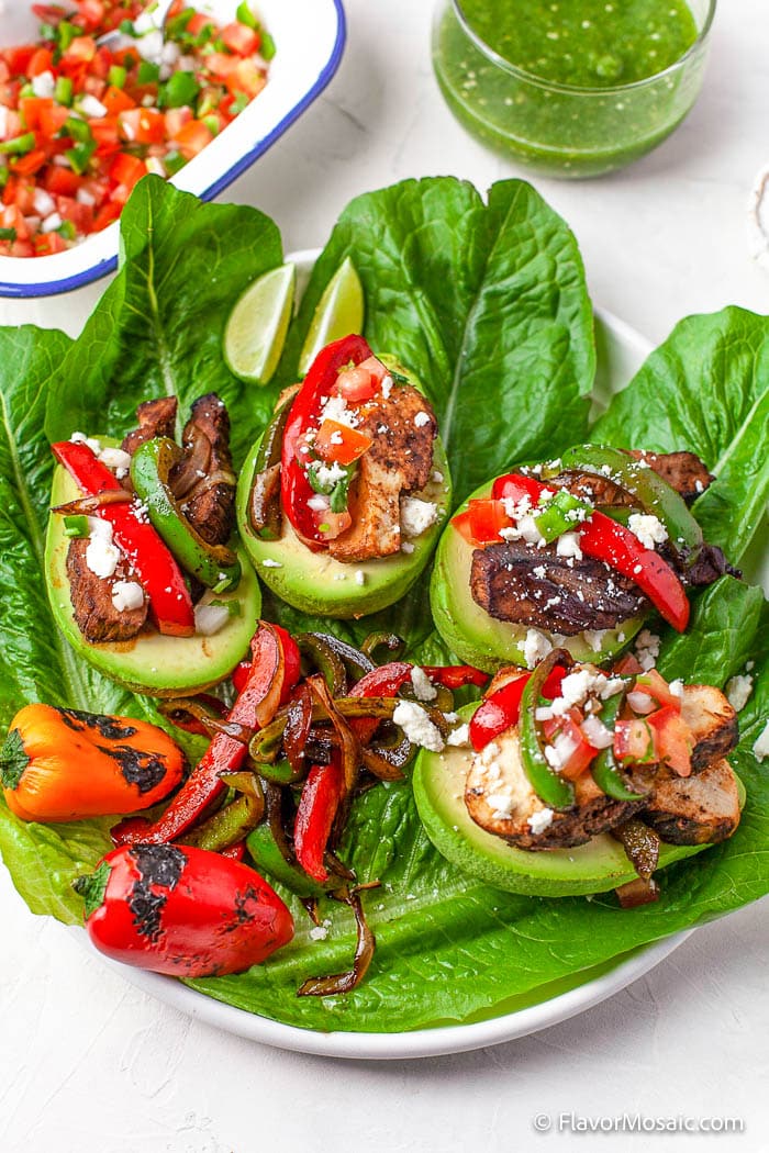 Overhead view of a plate with large lettuce leaves topped with Fajita Stuffed Avocados, sauteed red and green bell peppers