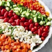 Photo of a rainbow salad with the individual ingredients separated in rows on top of the salad in a rustic white bowl.