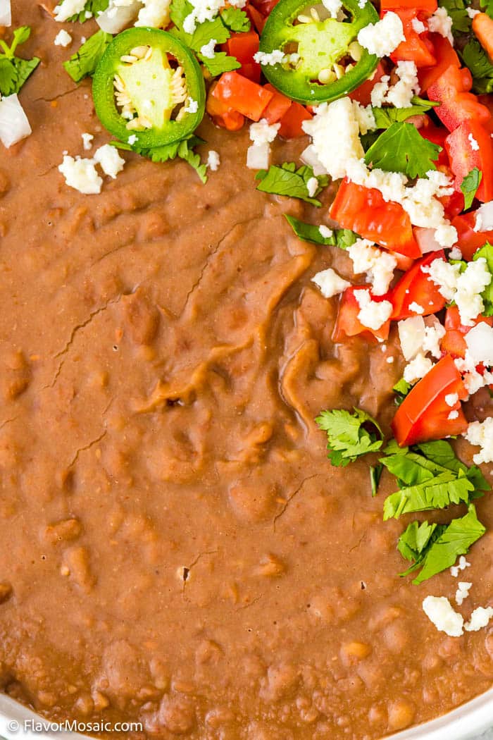 Close up of Refried beans with chopped cilantro, tomatoes, queso fresco, sliced jalapeños.