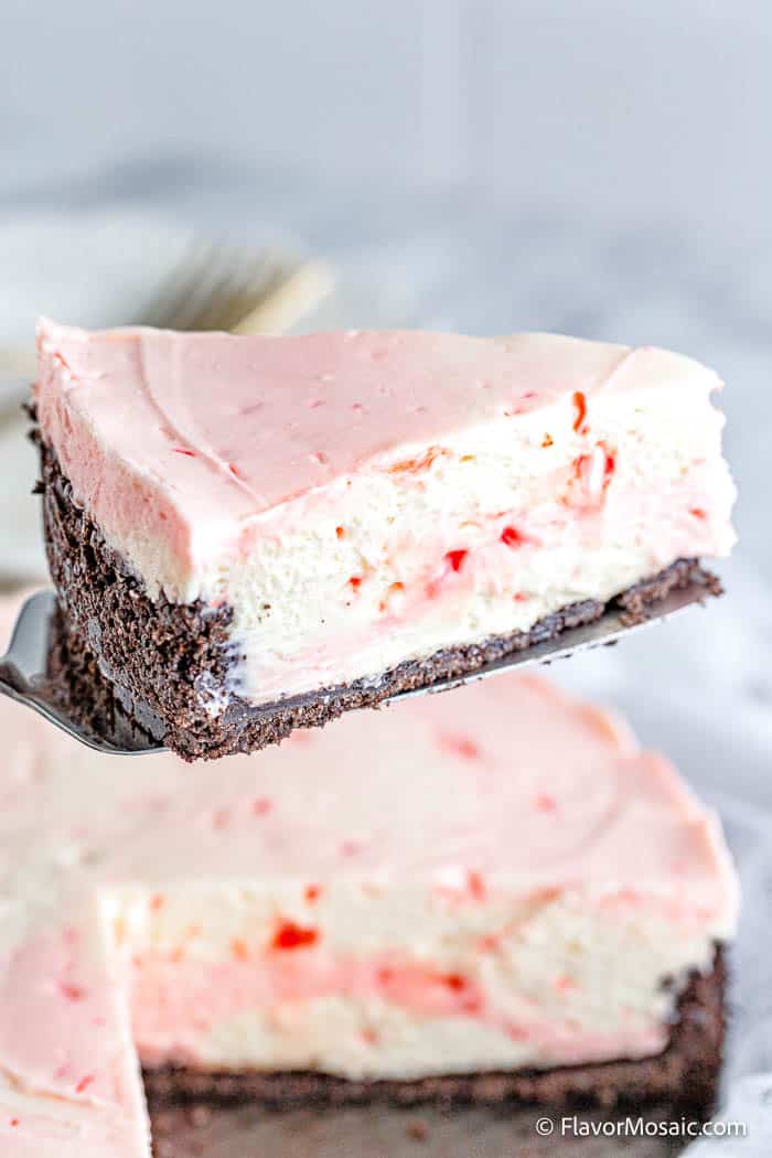A slice of No Bake Peppermint Cheesecake AKA Candy Cane Cheesecake is held over the rest of the cheesecake.