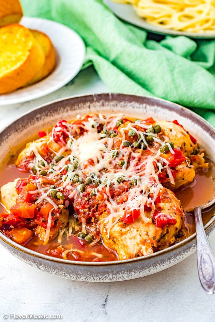 A large bowl of Instant Pot Saucy Italian Chicken with 4 chicken breasts covered with the Italian sauce and topped with mozzarella cheese and capers.