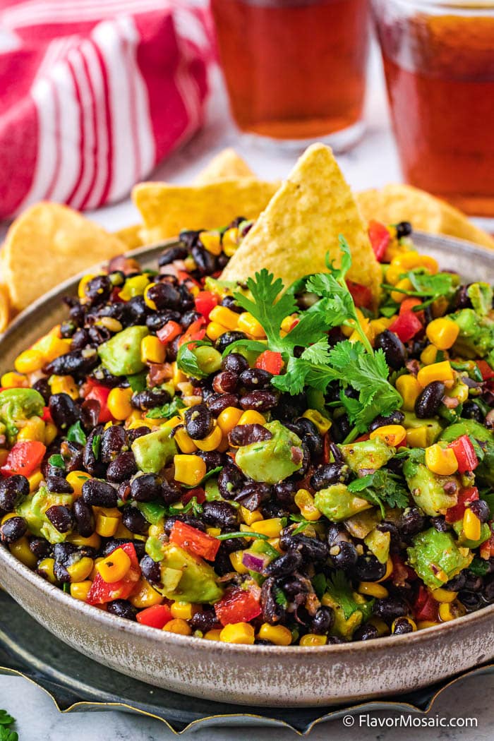 A large bowl of Mexican Corn and Black Bean Salad with tortilla chips ready to dip.
