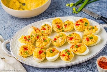 horizontal photo of a platter of pimento cheese deviled eggs garnished with pimentos and green onions.