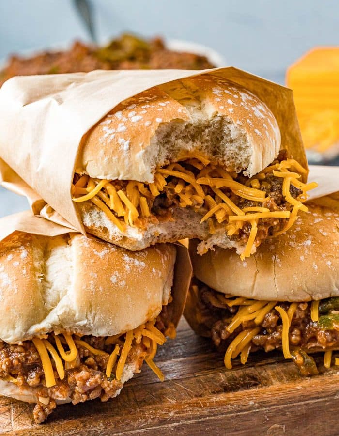 Photo of 3 brown paper-wrapped sloppy joes with shredded yellow cheese.
