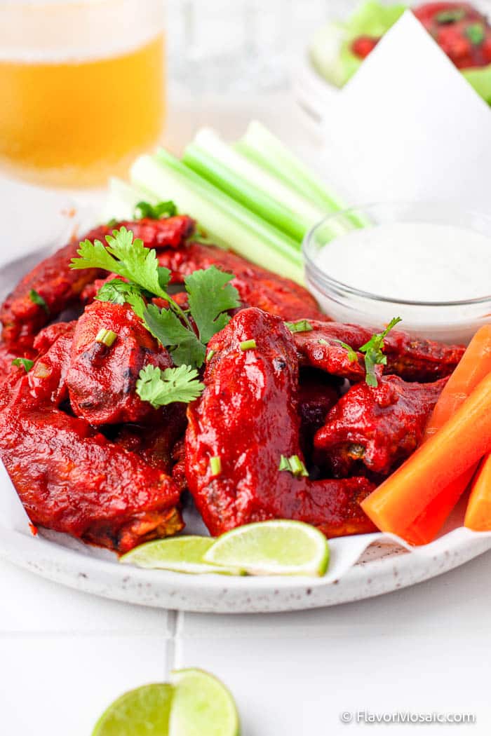 Side view of small plate of Air Fryer Honey Hot Wings Chicken Wings topped with Cilantro, with 2 small lime slices, carrot and celery sticks on the side next to a small glass bowl of ranch dressing.