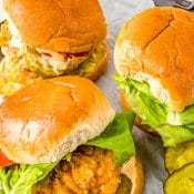 3 crispy chicken sandwiches topped with lettuce and tomatoes with pickles on the side.
