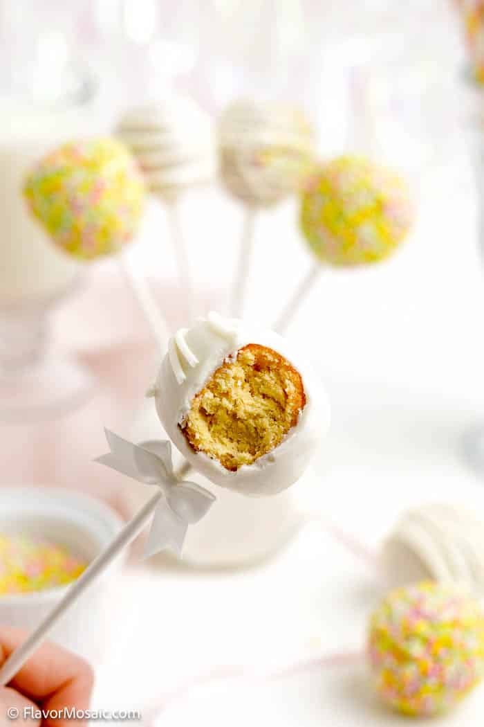 White chocolate covered donut hole cake pop with a bite taken out of it. Blurred whole cake pops in the background.