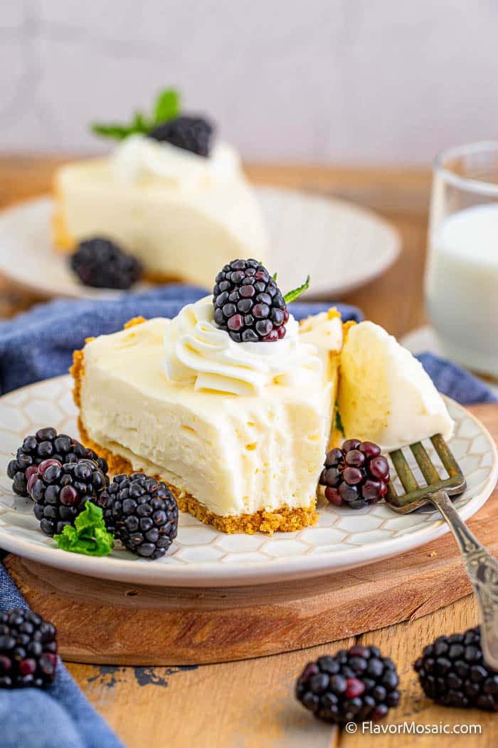 A single slice of pie on a dessert plate with a bite of cheesecake on a fork next to the cheesecake slice. Topped and surrounded by blackberries.