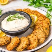 Plate of salmon patties with a dill dip surrounded by parsley and lemon.