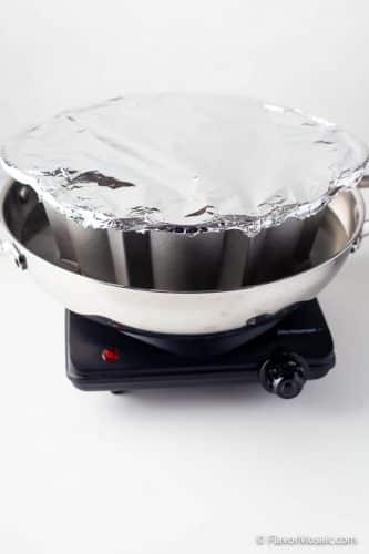 Foil covered bundt pan sitting in a larger pot sitting on a hot plate.