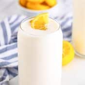 Side view of a glass of Chick Fil A Copycat Frosted Lemonade with a blue and white napkin in the back with a bowl of lemon sliced behind that.